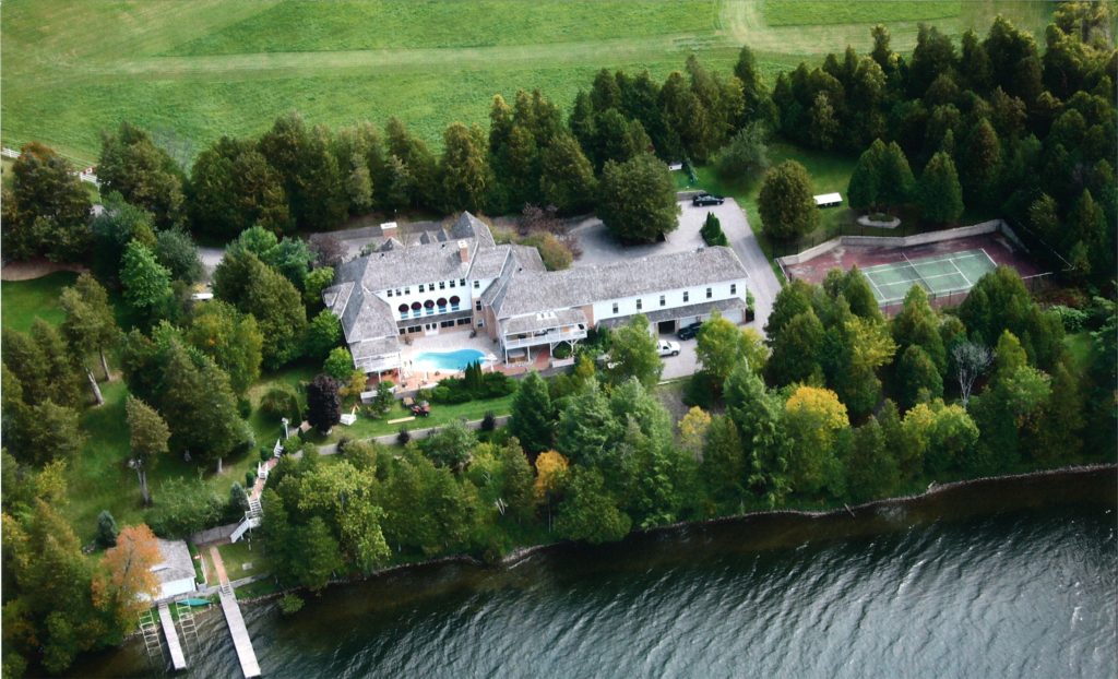 A large house with a pool and tennis court sits on the edge of a river. 