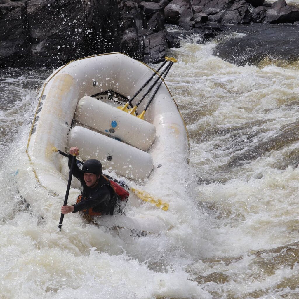 James Watt paddles a whitewater raft through intense rapids.