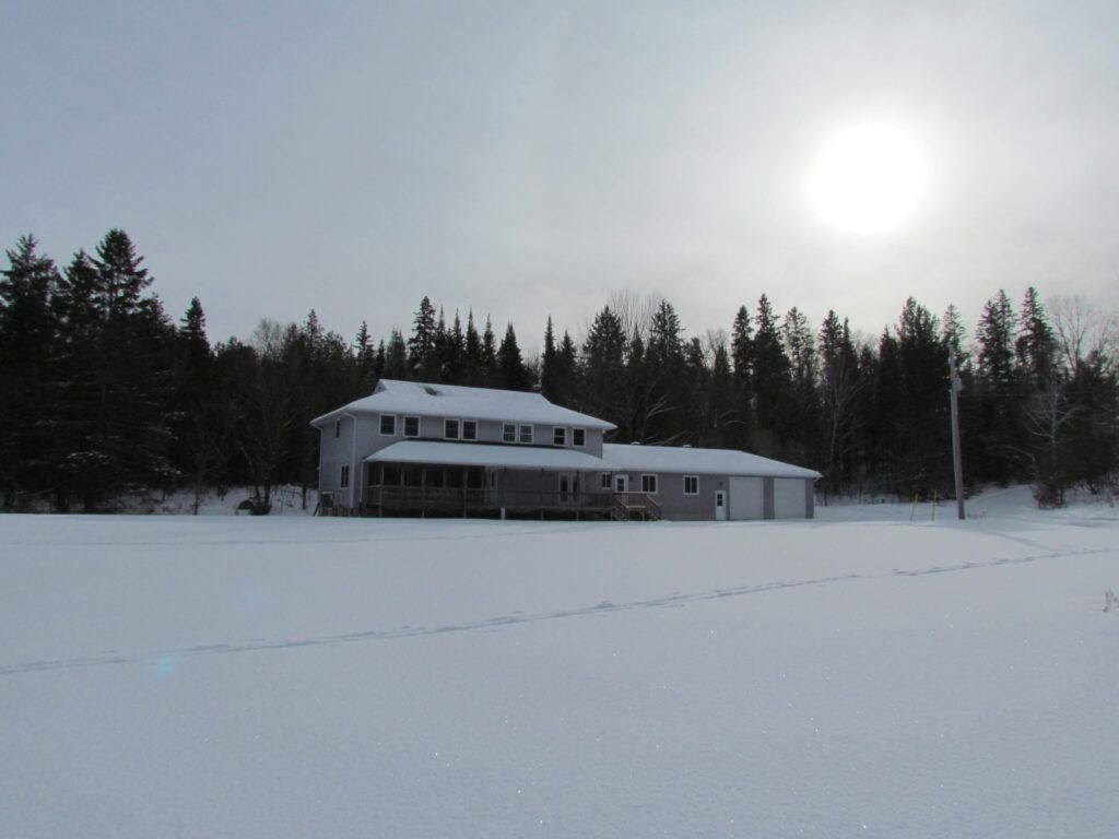 A large house covered in snow, on the edge of a forrest. 
